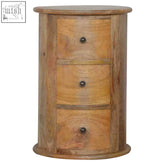 A rustic light brown wooden cylindrical nightstand with three drawers and dark metal knobs made of solid mango wood