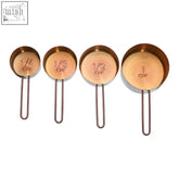 Set of four rose gold measuring cups with engraved capacity markings and loop handles in copper tone