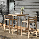 Light-colored wooden altro high bar table with two stools set outdoors against a gray siding wall