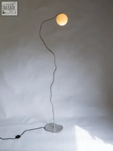 A sleek silver aluminium pea head floor lamp with a wavy metal stem and glowing spherical bulb