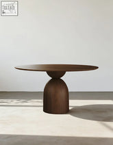 A sleek dark brown solid wood amaia round pedestal dining table with a rounded top and sculpted base