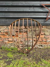 Rusty antique cast iron corner hay feeder with vertical bars and curved shield shape for livestock or garden use