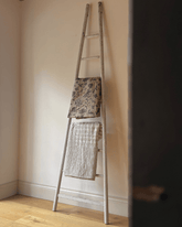 Weathered antique decorative ladder in chippy white paint with two patterned blankets draped over rungs