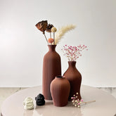 Three terracotta bara vases with vertical ribbed texture holding dried floral arrangements