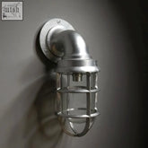 Industrial-style wall light with galvanized metal body and clear glass cage for outdoor and bathroom use