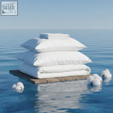 White organic cotton satin bed sheet set with neatly folded sheets and pillows on wooden platform in calm blue water