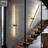 Modern gold-toned wall light with cylindrical accents illuminates concrete staircase perfect for warm bedroom lounge