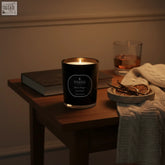 Black parks london black magic scented candle with gold rim lit on wood table featuring bright citrus and creamy vanilla