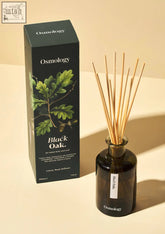 Dark amber glass reed diffuser with slender wooden sticks and minimalist black oak label by osmology for consistent fragrance throw and middle notes