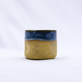 A bluvia goccia handmade ceramic stoneware cup with a speckled tan body and vibrant blue glazed rim
