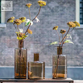 Three mouth blown bottle vases from dutz collection in amber topaz glass holding dried yellow flowers with slender stems
