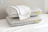 Gray geometric-patterned eclipse pillow with dark piping and yellow tags topped with folded white eucalyptus silk pillowcase