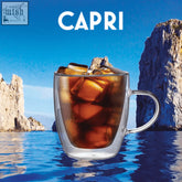 A capri double walled glass mug with sturdy handle filled with iced coffee and ice cubes in dark amber liquid