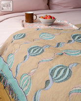 Beige throw blanket with teal and light blue embroidered leaves and fringed edge from micaela sharp collaboration