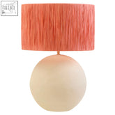 A natural papier mache table lamp with a coral pleated shade and matte off-white spherical base called carta natural