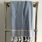 A light blue and navy fringed cotton fouta towel with white fringe and striped border hanging on a chrome rack