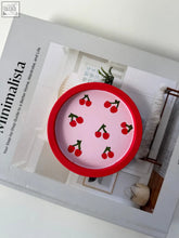 A round pink ceramic cherry trinket dish with a red rim and small red cherry illustrations perfect for holding small items