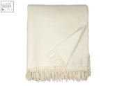 Cream-colored clova merino lambswool throw blanket with soft textured weave and fringe perfect for cozy nights