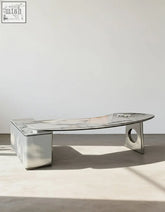 Modern metallic coffee table with curved glass top and angular legs paired with coelho corner office desk sintered stone