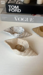Beige speckled ceramic conch shell trinket dish holding gold rings for stylish jewelry storage