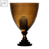Amber-colored hammered glass candle holder with a dark wooden base perfect for cozy glass candle displays