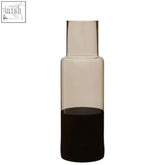 A sleek smoked glass bottle vase with a narrow neck and dark amber liquid in the cova smoked glass bottle