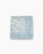 Folded cranberry blue and white hand blocked tablecloth with blue green floral pattern and navy scalloped edge