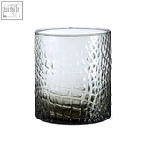 A clear glass tealight holder with a crocodile-skin pattern and dark smoked glass base perfect for candles