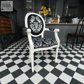A white ornate bowler arm chair by dan gold with black skull and barrettes upholstered back and seat