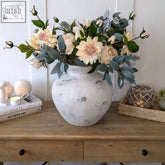 A darcy antique white ceramic vase with a distressed finish holds cream and blush pink flowers with sage foliage
