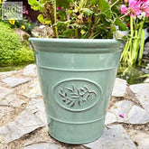 Matte sage green ceramic effect plastic planter with embossed leaf motif holding vibrant pink and yellow flowers
