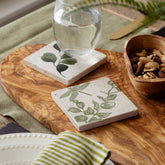 Two off-white natural limestone stone coasters with green botanical and dragonfly prints heat resistant design