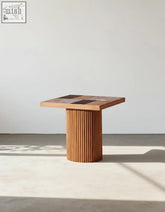 D’Souza square side table combines solid wood with a ribbed pedestal base and patchwork light and dark wood top
