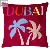 A vibrant red dubai needlepoint cushion with embroidered multicolored dubai text and two stylized palm trees