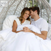 White wicker hanging chair with cage-like design shown with eucalyptus silk duvet upgrade bundle in white