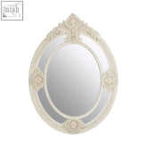An ornate oval eclipse antique white mirror with a distressed frame and intricate floral scrollwork design