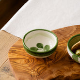 A small ceramic dip bowl with a green rim and hand painted leaf design featuring a white interior