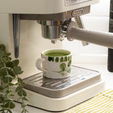 White ceramic espresso cup with hand painted green leafy pattern under a coffee machine for easy use