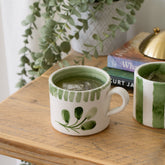White ceramic mug with hand painted green botanical design and striped rim filled with iced tea ceramic mug