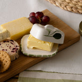White ceramic mini ceramic butter dish with green leaf and olive design and matching lid covering yellow butter