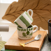 White ceramic flora stripe 2 espresso cups with hand painted green stripes and leaf motifs stacked on wooden board