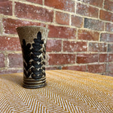 A floral ceramic vase with speckled beige glaze and black leafy patterns on a textured yellow surface