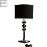 Black fredman table lamp with black cylindrical shade and three chrome spheres on a sleek gunmetal base