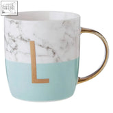 A ceramic mug with a frosted deco marble effect top half and pastel green bottom featuring a gold l monogram