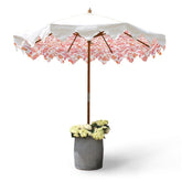 A garden umbrella with a hand block printed white canopy pink floral pattern scalloped edge and wooden pole