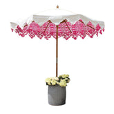 A garden umbrella with a hand block printed canopy in white featuring pink floral patterns and a wooden pole