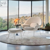 Cream-colored upholstered george womb chair with sleek metal legs and matching ottoman for cozy seating