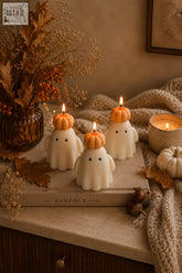 Three white ghost candles with orange pumpkin hats and lit wicks made from natural soy wax for halloween decor