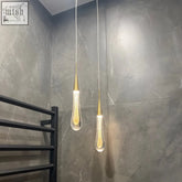 Two gold-toned glass drop pendant lights with teardrop glass shades filled with golden glitter against gray marble