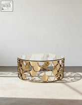 A modern gold nesting coffee table with a clear glass top and an ornate gold metal base with scale patterns